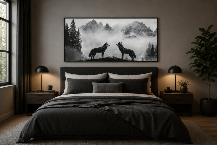 Black and white framed canvas wall art of two wolves on a cliff in foggy mountains above a bed.