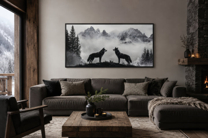 Black and white framed canvas wall art of two wolves on a cliff in foggy mountains above a sofa.