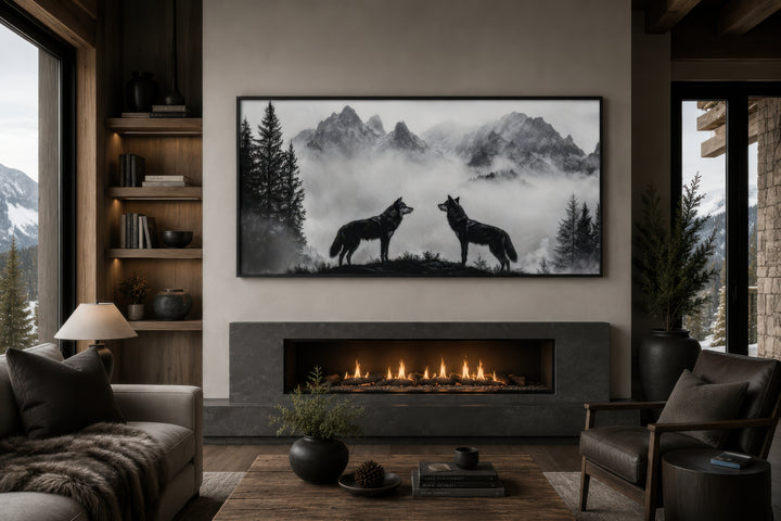 Black and white framed canvas wall art of two wolves on a cliff in foggy mountains above a fireplace