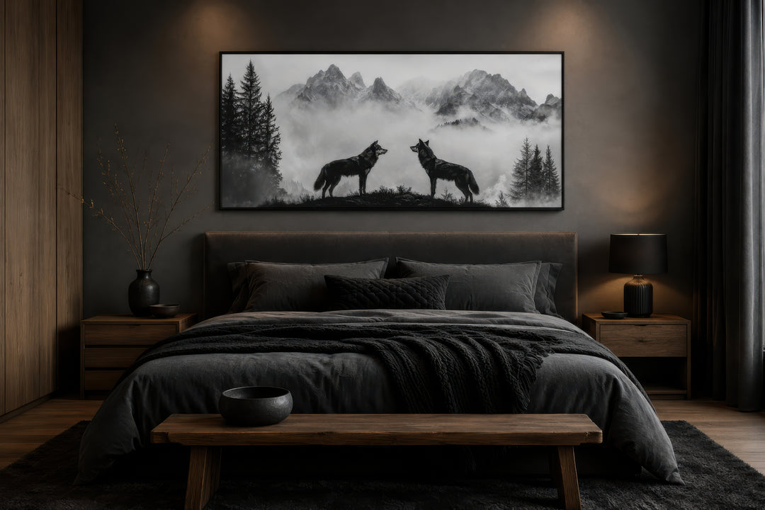 Black and white framed canvas wall art of two wolves on a cliff in foggy mountains above a bed.