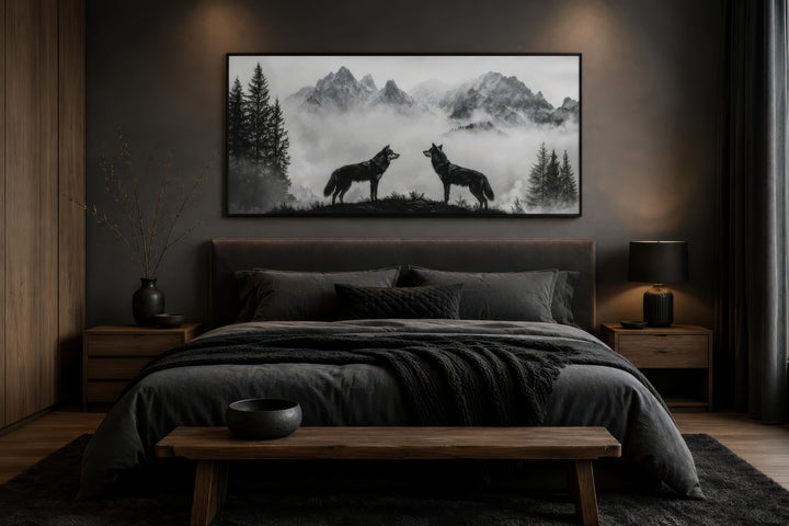Black and white framed canvas wall art of two wolves on a cliff in foggy mountains above a bed.