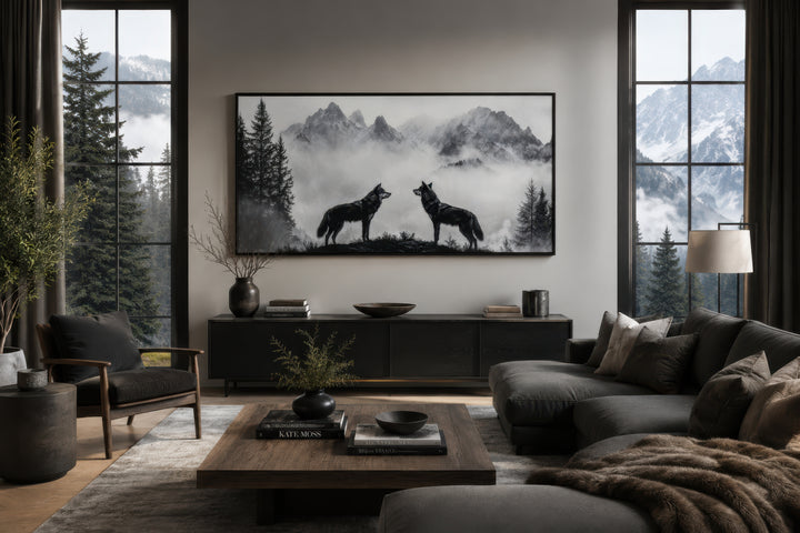 Black and white framed canvas wall art of two wolves on a cliff in foggy mountains above a console.