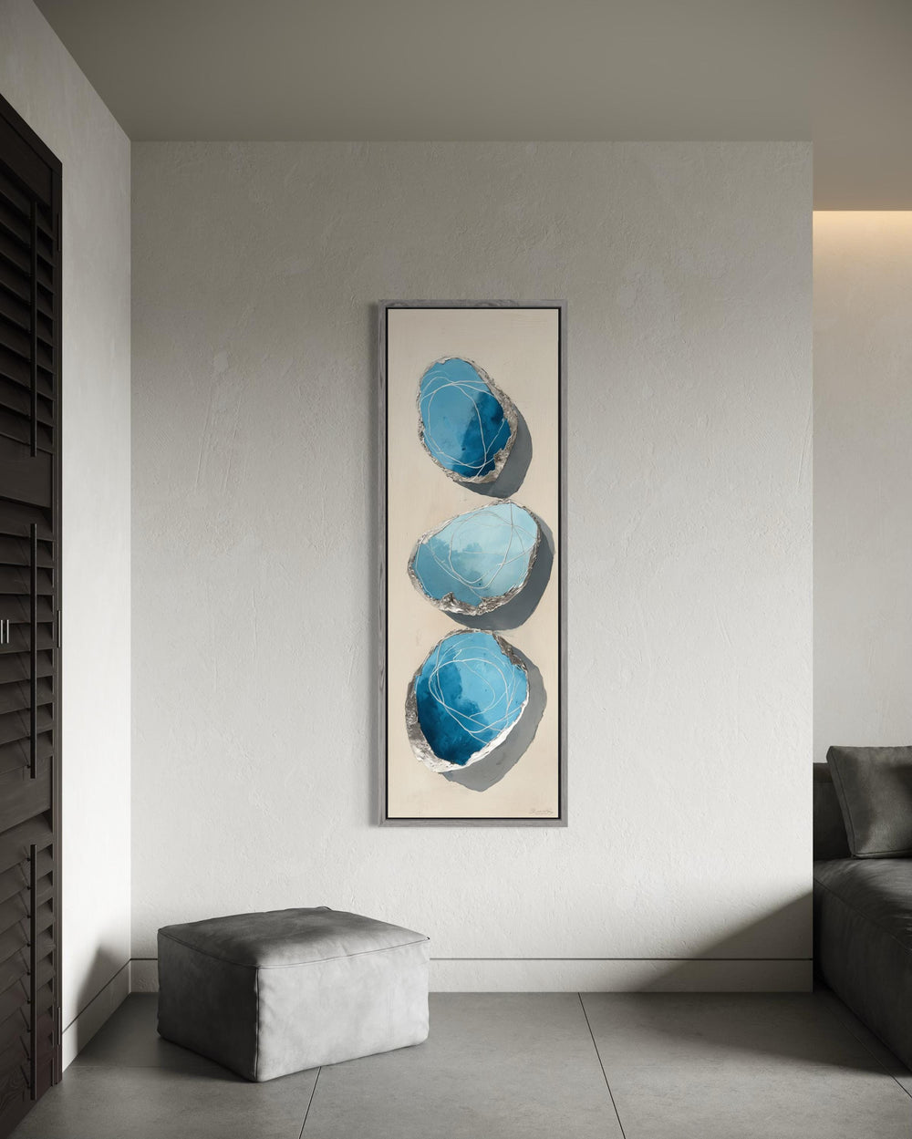 Vertical tall narrow canvas print featuring three abstract blue and silver stones on a neutral wall.