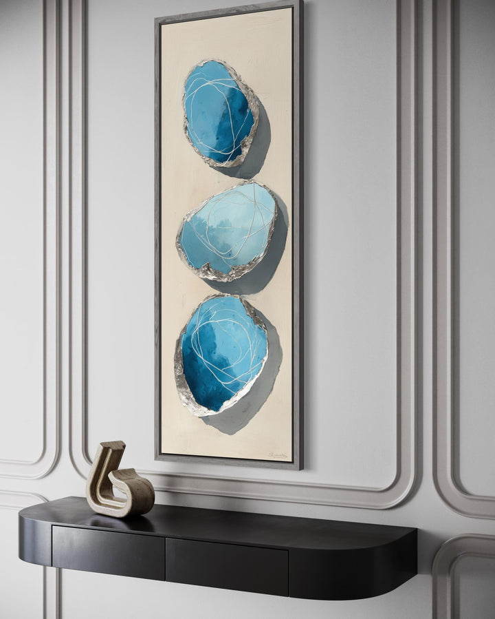 Vertical abstract canvas print featuring three blue and silver stones on a tall, narrow frame.