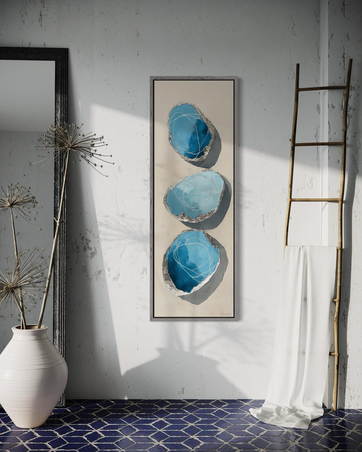 Vertical tall narrow canvas print featuring three abstract blue and silver stones on a neutral wall.