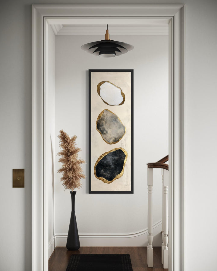 Vertical abstract wall art featuring three stacked black, white, and grey rocks with gold edges.
