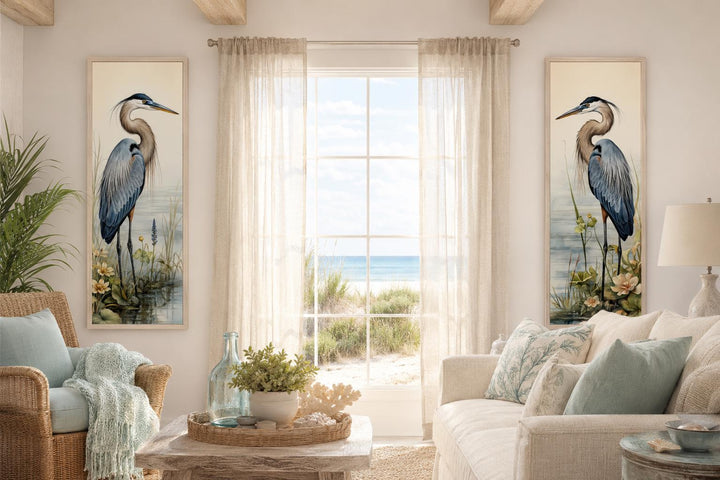 Two vertical canvas prints of Great Blue Herons in a coastal living room flanking a window.