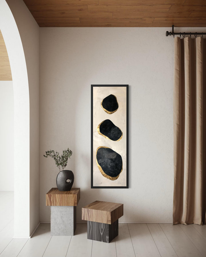 Vertical tall narrow wall art featuring three abstract black and gold rocks in a black frame.