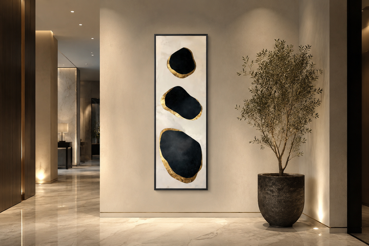 Vertical wall art with three black and gold abstract rock shapes on a neutral textured background.