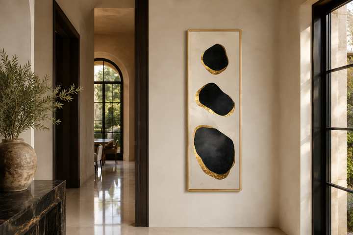 Vertical tall narrow wall art with three abstract black and gold rock shapes in a modern entryway.