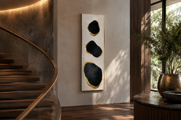 Vertical tall narrow wall art with three black and gold abstract rock shapes in a modern entryway.
