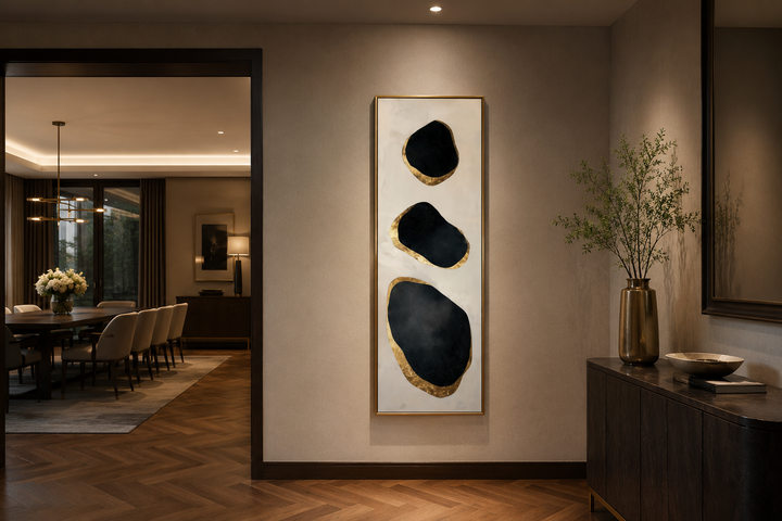 Vertical tall narrow wall art with three abstract black and gold rock shapes in a modern entryway.