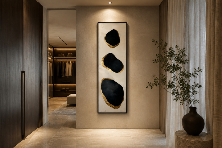 Vertical tall narrow wall art with three black and gold abstract rock shapes in a modern entryway.