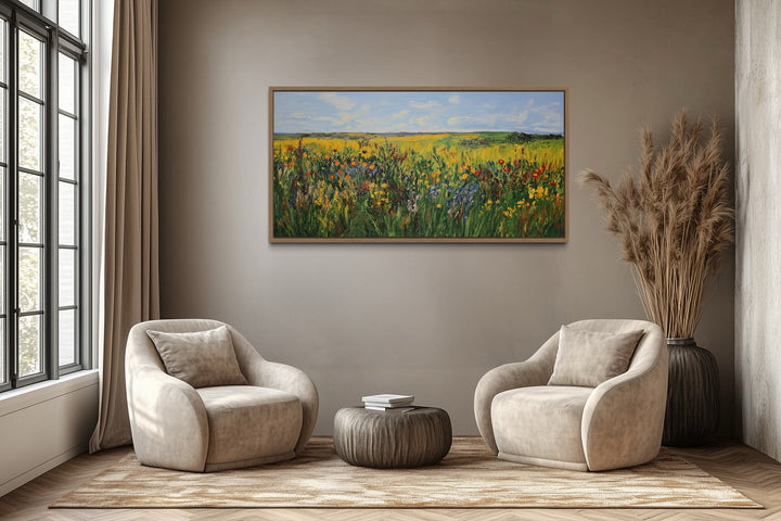 Vibrant impressionist wildflower meadow framed canvas wall art above two chairs in a living room.