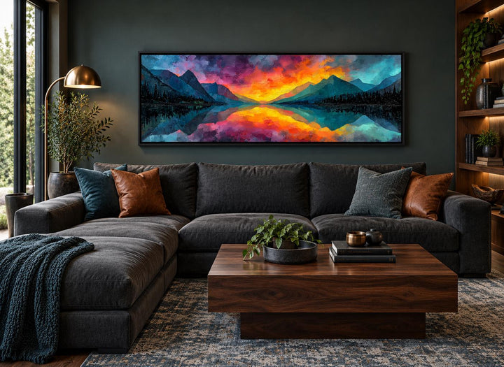 Vibrant mountain lake sunset panoramic canvas art above a dark sofa in a modern living room.