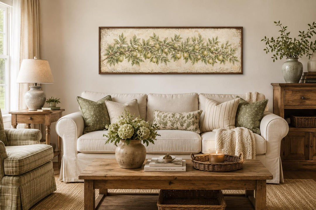 Long narrow vintage botanical canvas painting of a green apple branch above a white farmhouse sofa.
