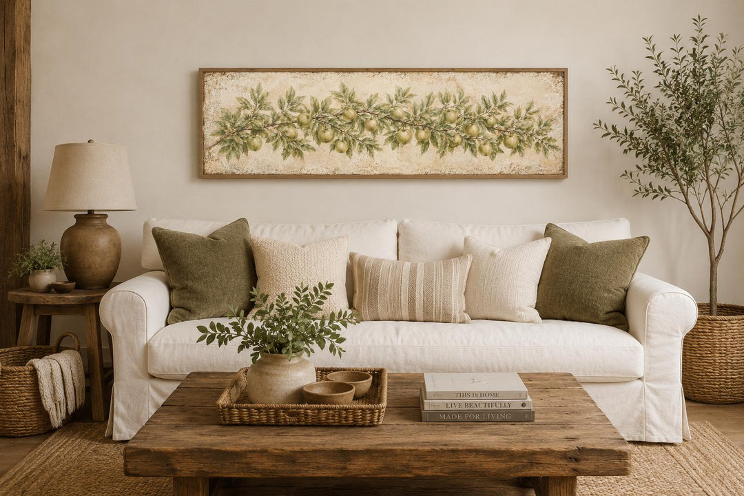 Long narrow vintage botanical canvas featuring a green apple branch above a white farmhouse sofa.