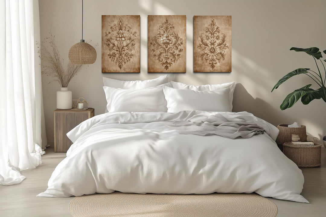 Set of three vintage damask wall art canvases with neutral beige ornamental patterns over a bed.
