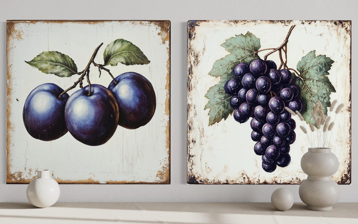 Set of two rustic botanical canvas prints featuring realistic plums and grapes on aged backgrounds.