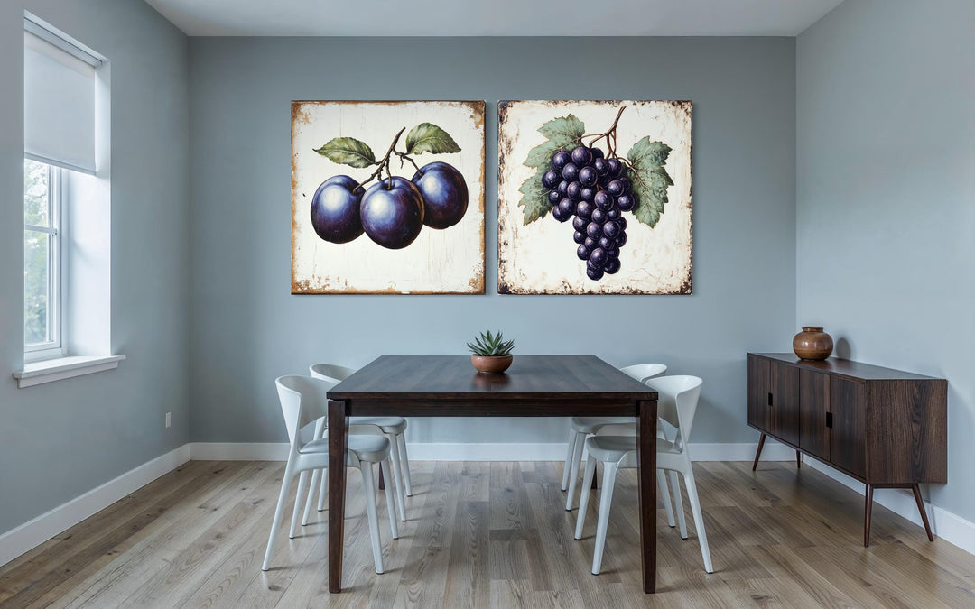 Set of two rustic botanical canvas prints featuring vintage-style plums and grapes on a gray wall.