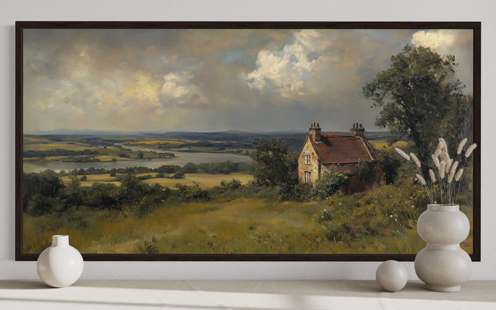 Vintage framed canvas wall art of an old house near a river in a wide rural landscape.