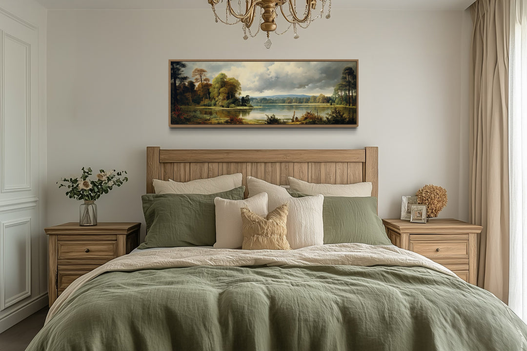 Vintage landscape painting of a lake and forest in a narrow horizontal frame above a bed.