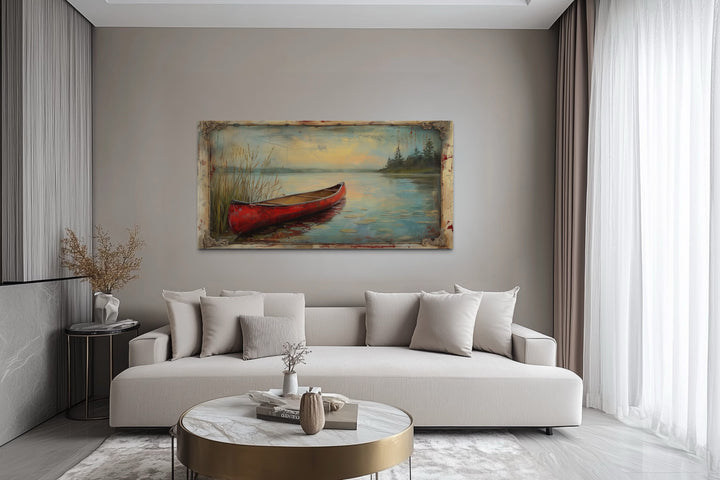 Vintage red canoe lake painting in a rustic frame hanging above a modern sofa in a living room.