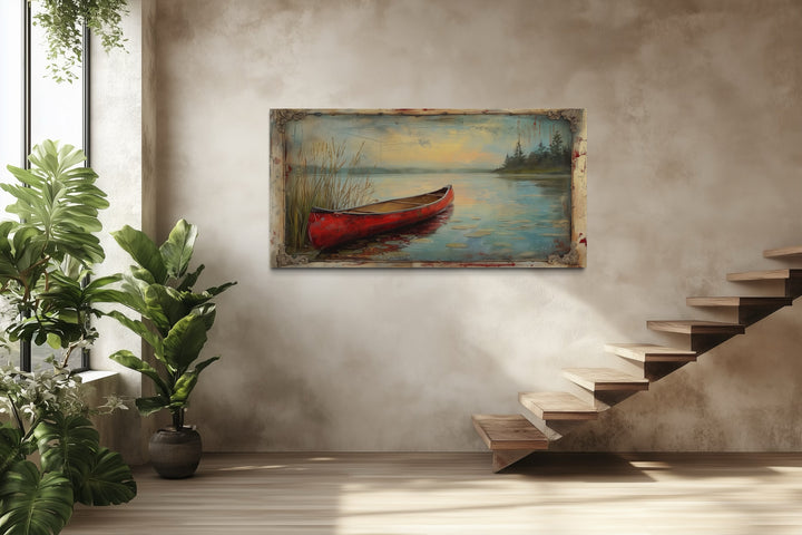Vintage red canoe lake painting in a rustic frame on a neutral wall near wooden stairs.