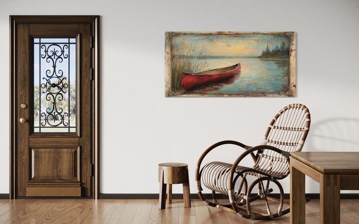 Vintage red canoe lake painting in a rustic frame hanging on a white wall in a cabin-style room.