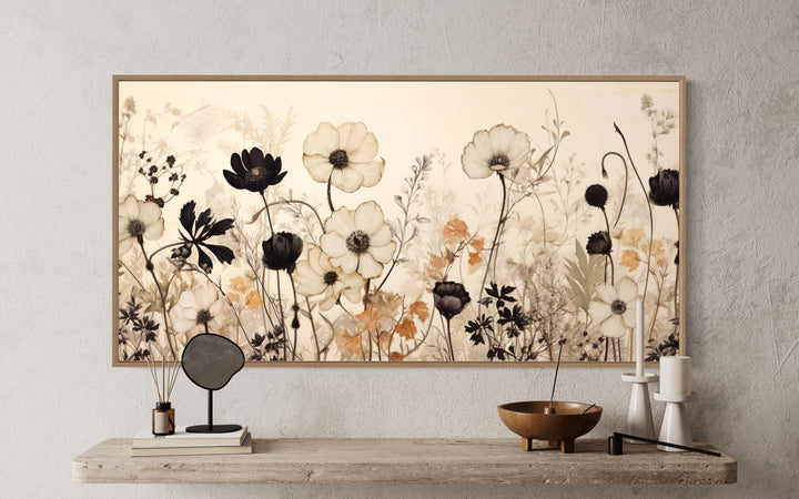 Vintage black and neutral wildflower canvas wall art in a wood frame above a rustic shelf.