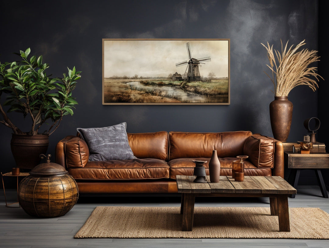 Vintage windmill canvas print in a rustic frame hanging above a brown leather sofa in a living room.