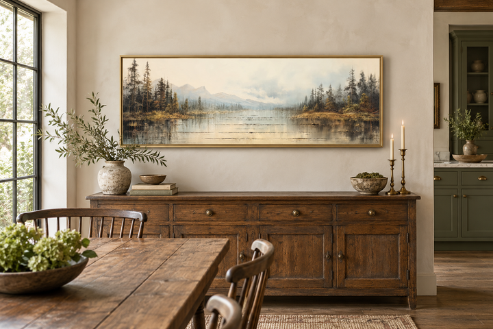 Vintage neutral lake landscape horizontal wall art in a gold frame above a rustic wooden sideboard.