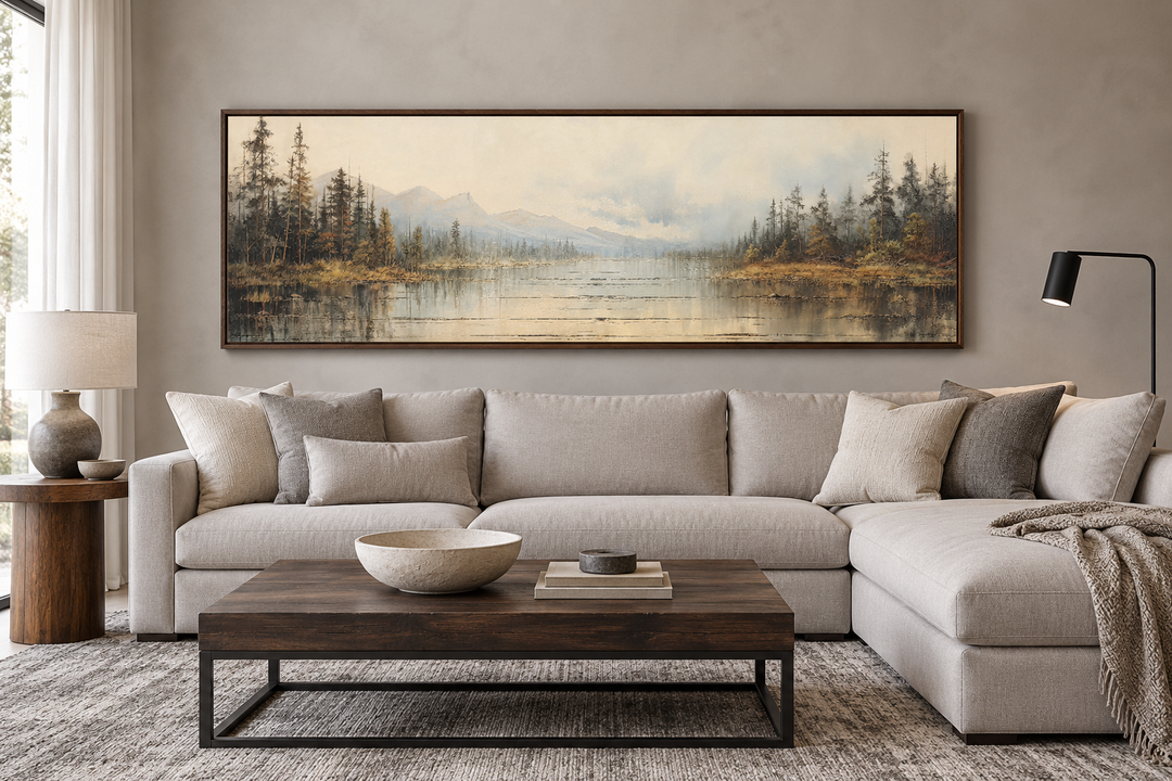 Vintage neutral lake landscape long horizontal wall art in a dark wood frame above a beige sofa.