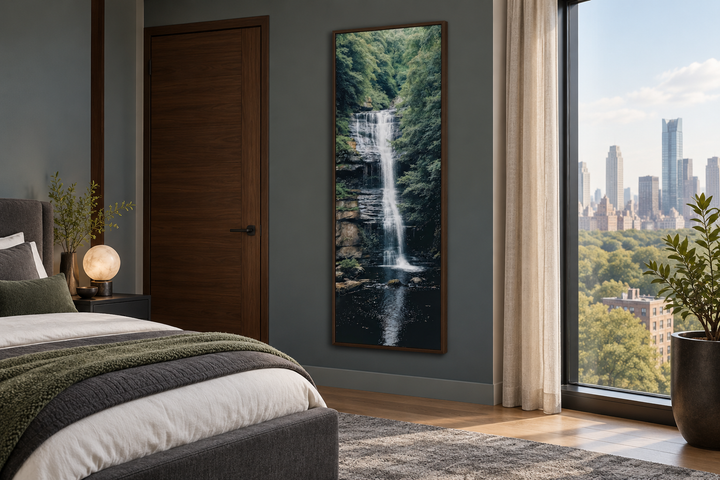 Tall narrow vertical framed canvas wall art of a waterfall in a forest, hanging in a bedroom.