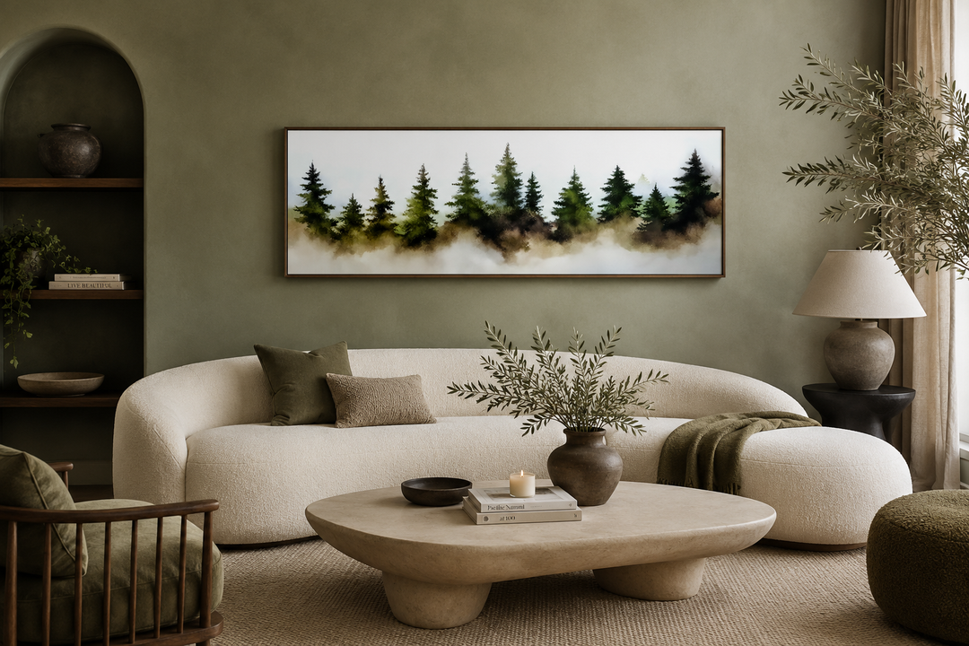Horizontal watercolor painting of foggy green pine trees in a forest, framed above a white sofa.