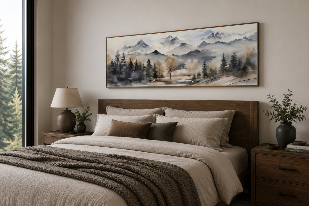 Framed horizontal canvas wall art of a watercolor mountain landscape in earth tones above a bed.