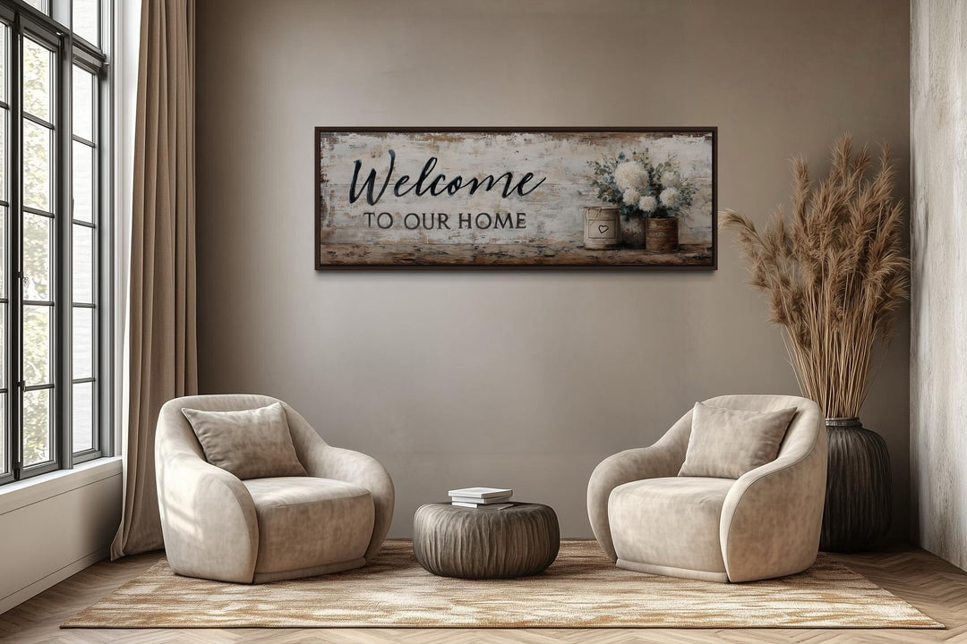 Welcome to Our Home long horizontal farmhouse wall art with flowers above two chairs in a room.