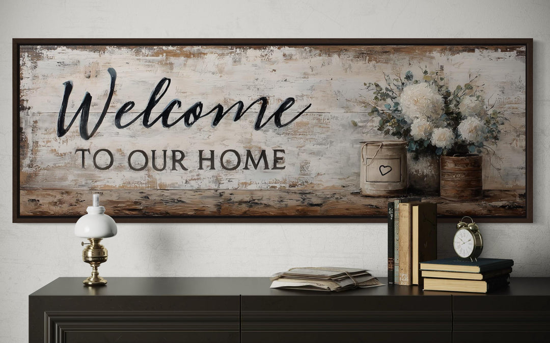 Farmhouse wall art with 'Welcome to Our Home' script and white flowers above a dark console table.