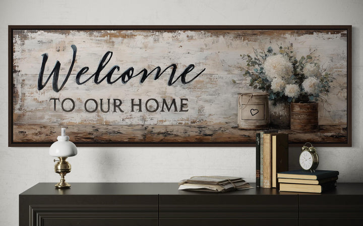 Farmhouse wall art with 'Welcome to Our Home' script and white flowers above a dark console table.