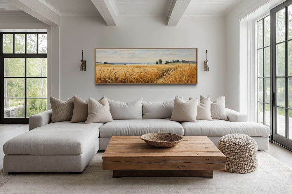 Long horizontal framed canvas wall art of a golden wheat field landscape above a living room sofa.