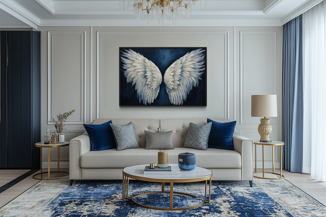 Framed canvas wall art of white angel wings on a dark blue background above a beige sofa.