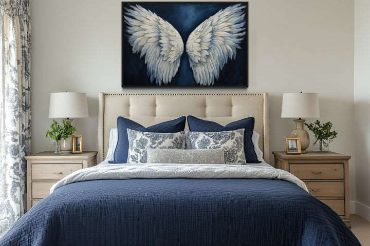 White angel wings on blue background framed canvas wall art hanging above a bed in a bedroom.
