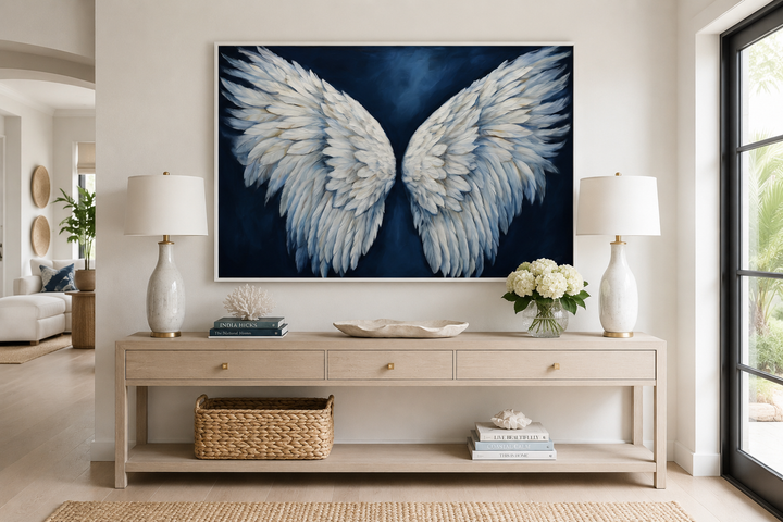 White angel wings on blue background framed canvas wall art above a console table in a living room.
