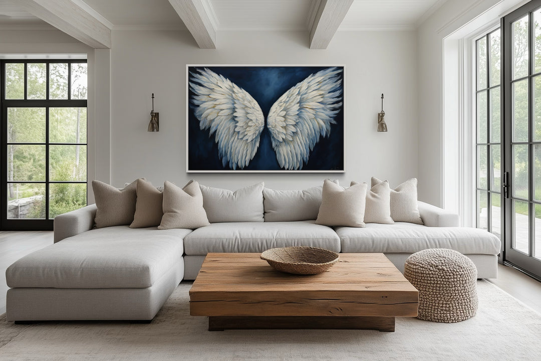 White angel wings on blue background framed canvas wall art above a neutral sectional sofa.