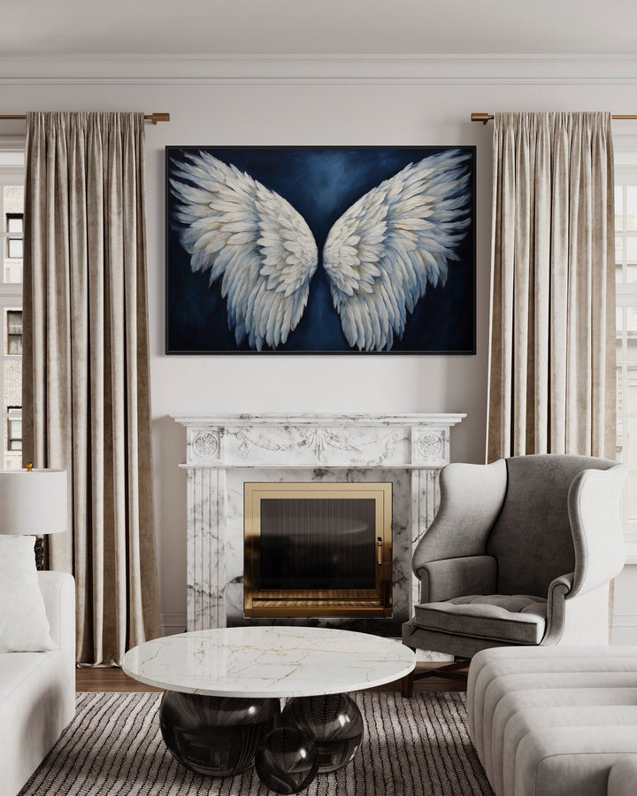 Framed canvas wall art of white angel wings on a dark blue background above a marble fireplace.