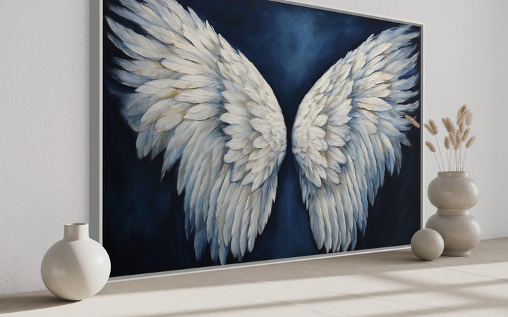 White angel wings on a dark blue background framed canvas wall art in a modern room setting.