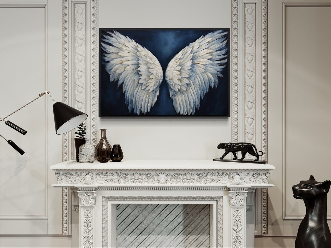 White angel wings on a dark blue background framed canvas wall art above a white fireplace mantel.