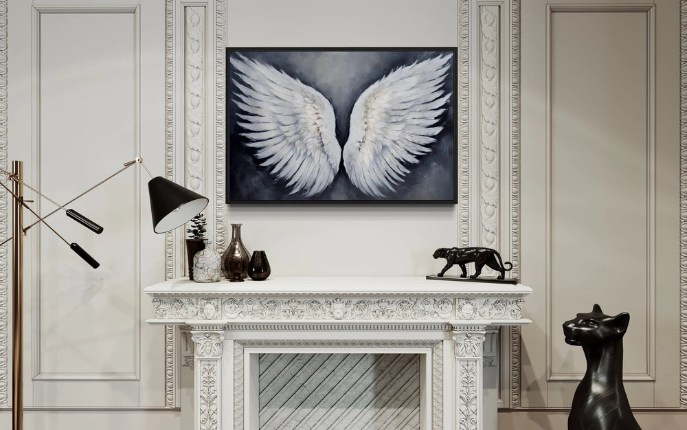 White angel wings on a grey background wall art framed above a white ornate fireplace.