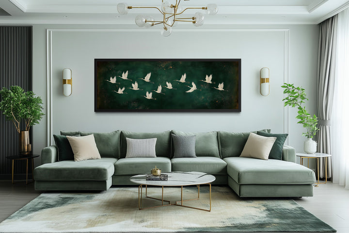 White birds flying across a long horizontal emerald green canvas wall art above a green sofa.