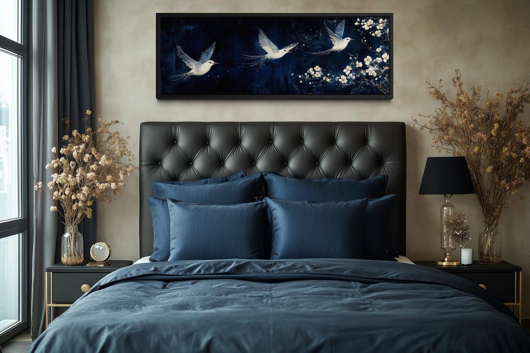 Long narrow canvas print of white birds and blossoms on a navy background above a tufted headboard.